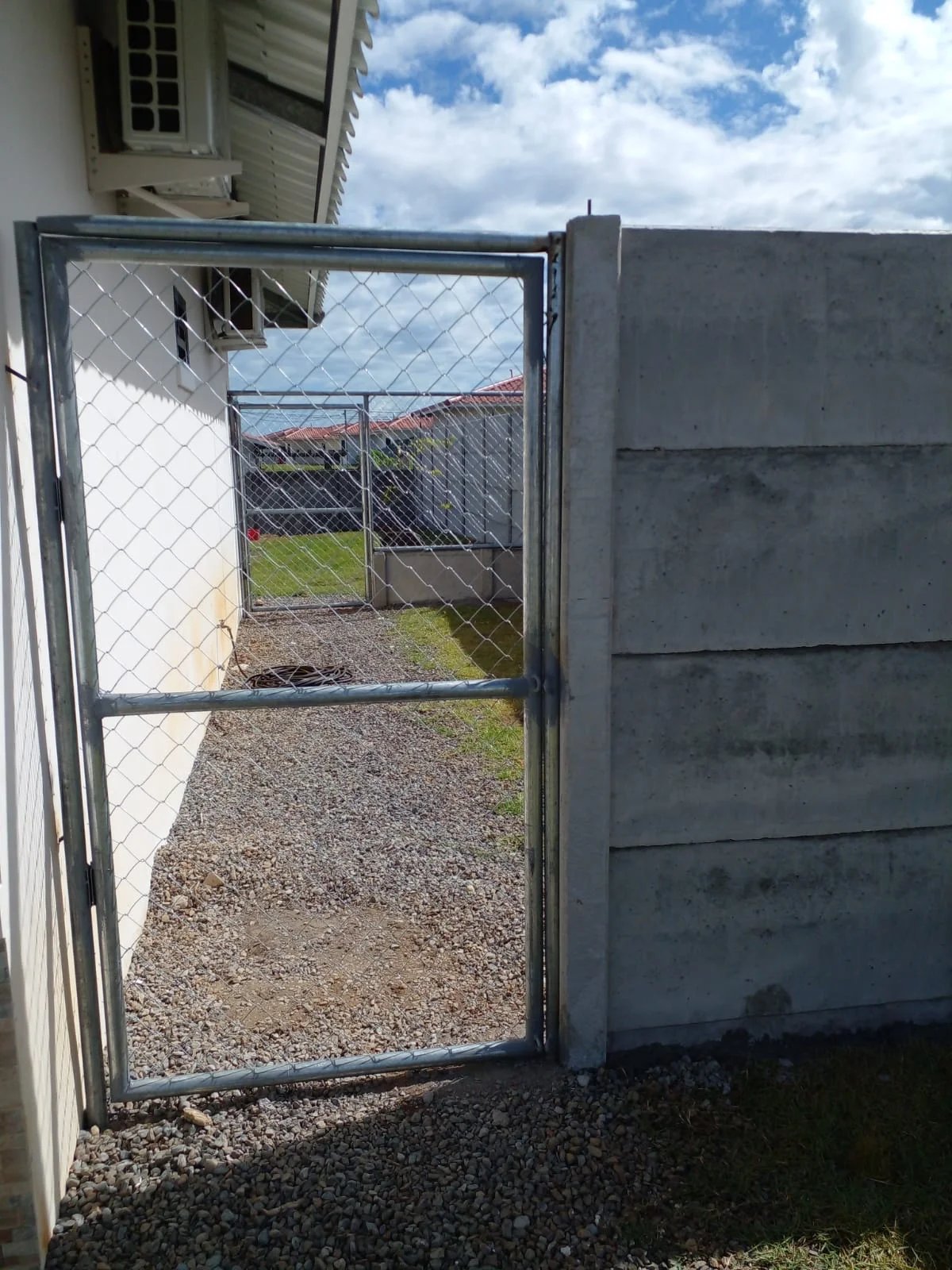Vista a través de portón metálico hacia patio interior con muro perimetral prefabricado al fondo