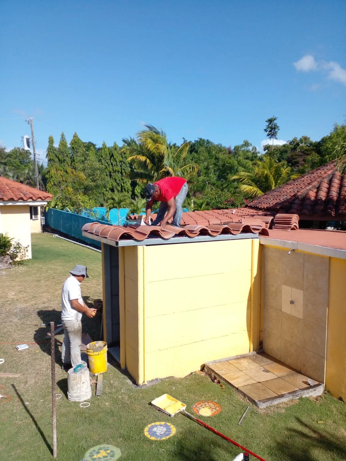 Operarios pintando techo de tejas y muro de quiosco amarillo en mantenimiento de área social