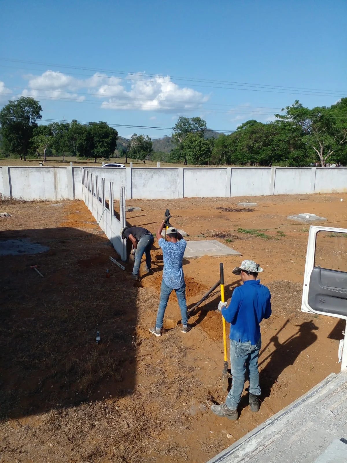 Cuadrilla instalando muro perimetral prefabricado en lote rural amplio con horizonte despejado