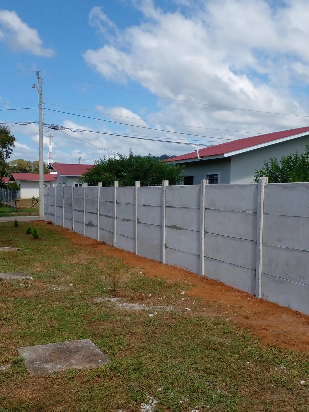 Muro perimetral prefabricado terminado delimitando lote en urbanización con residencia