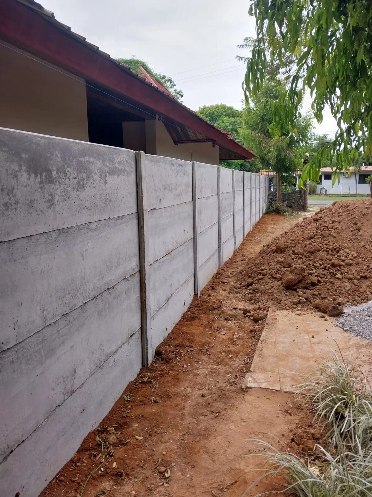 Muro perimetral prefabricado lateral con vivienda terminada y vegetación arbolada al fondo