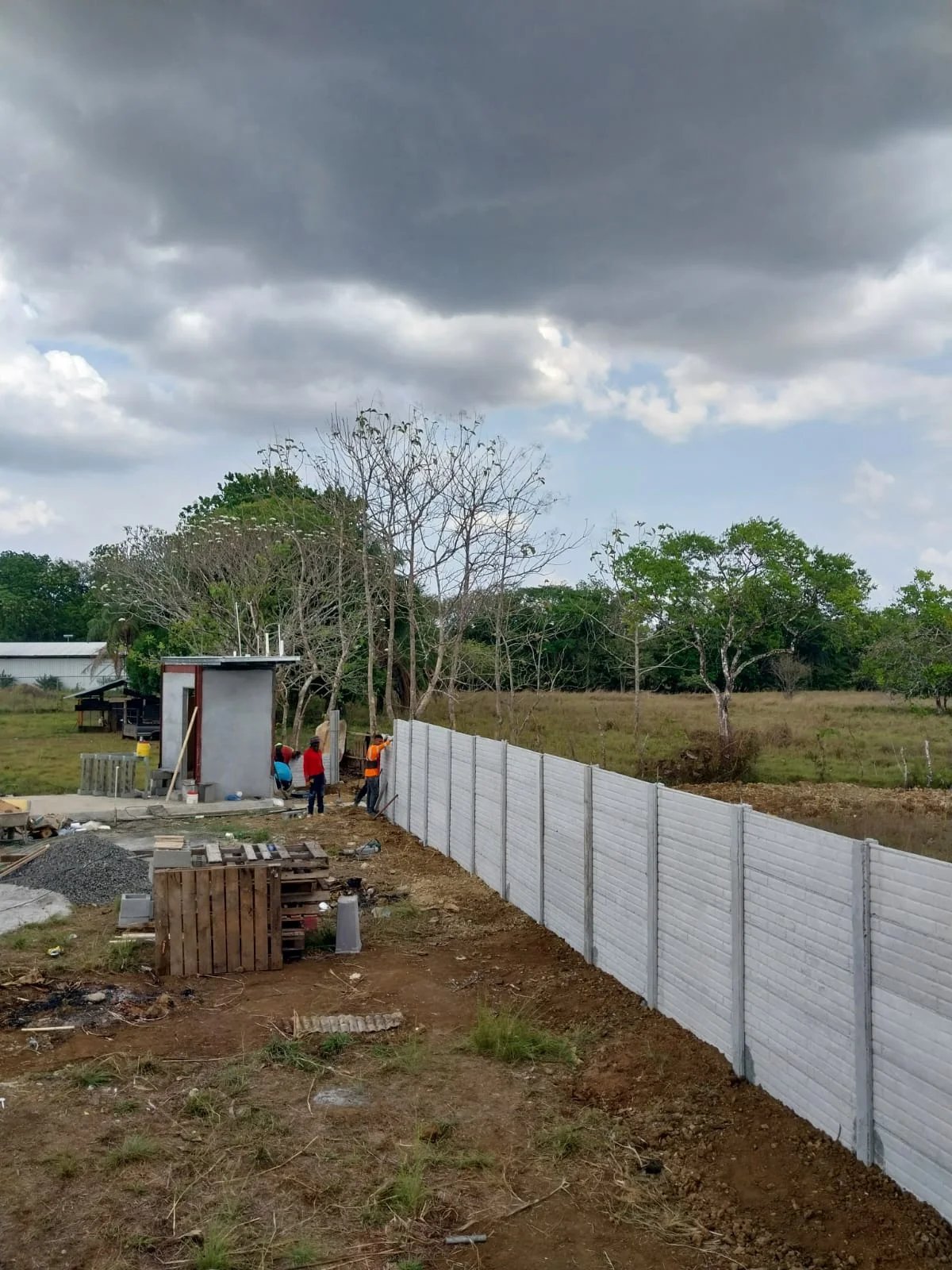 Muro perimetral prefabricado largo en lote rural con cielo nublado y horizonte abierto