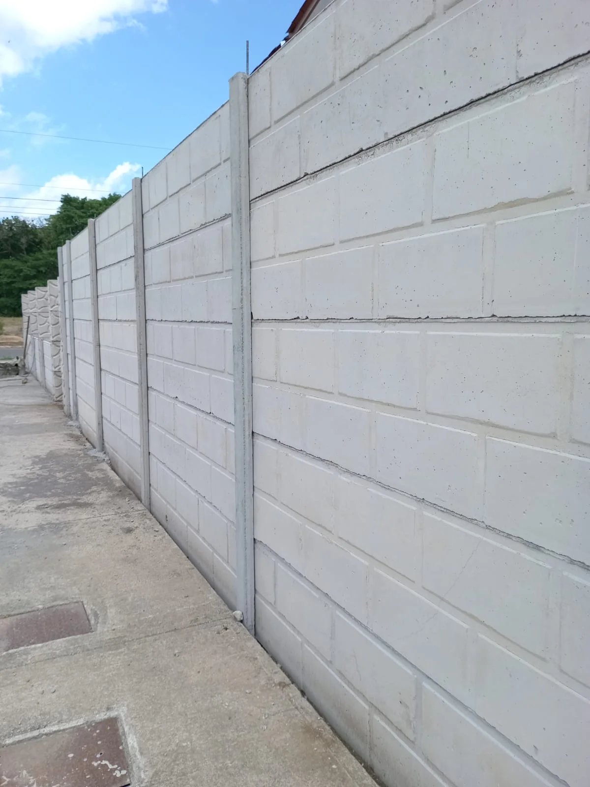 Muro perimetral con textura tipo bloque blanco y columnas en perspectiva sobre acera de concreto