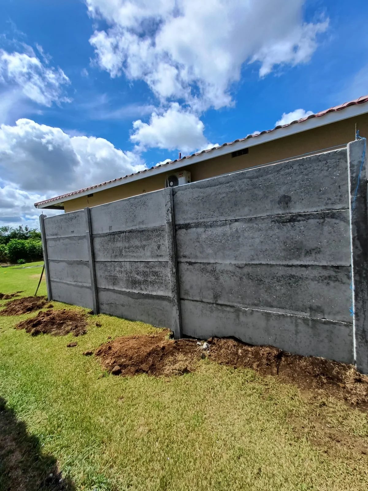 Muro perimetral lateral terminado con base de tierra removida y vivienda con techo rojo