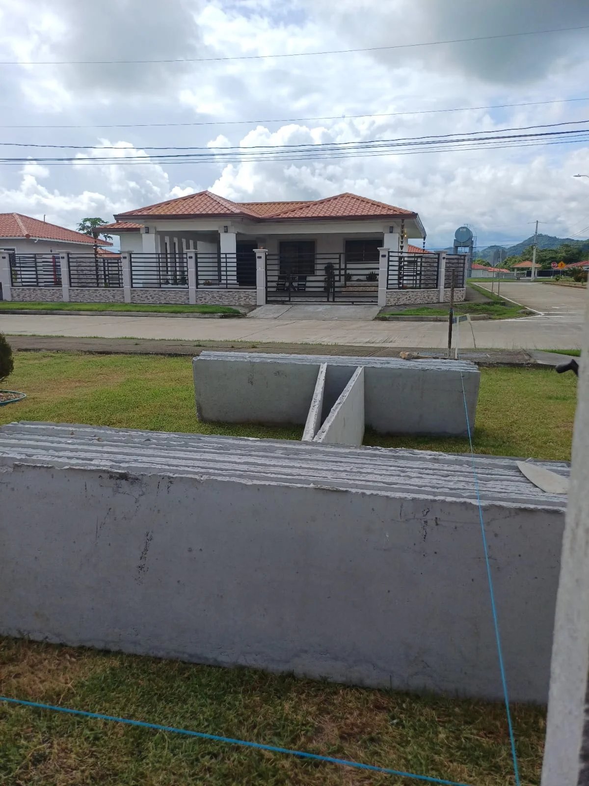 Paneles prefabricados apilados sobre acera frente a residencia con muro perimetral terminado