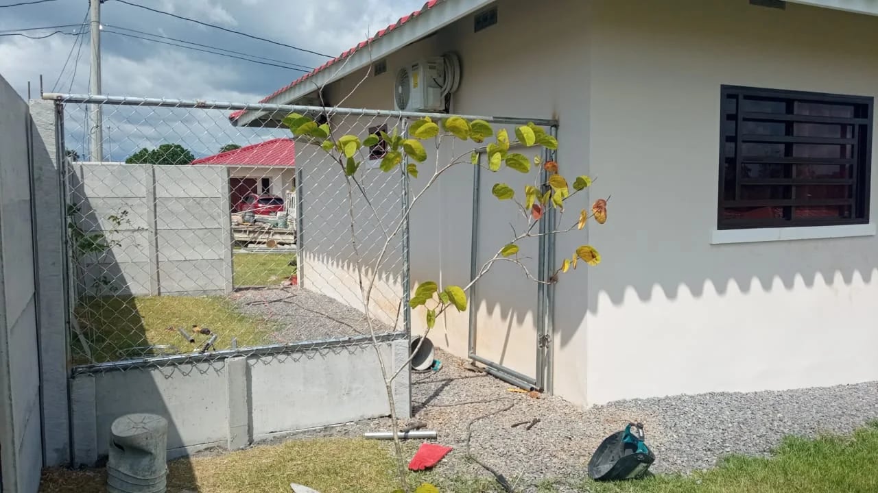 Cerca de alambre con portón metálico delimitando jardín de residencia con muro perimetral lateral