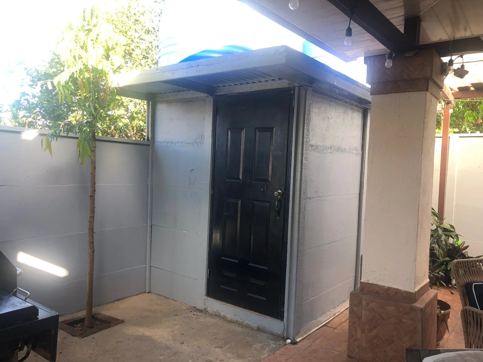 Pequeña bodega residencial con muros de concreto y puerta metálica negra en patio interior