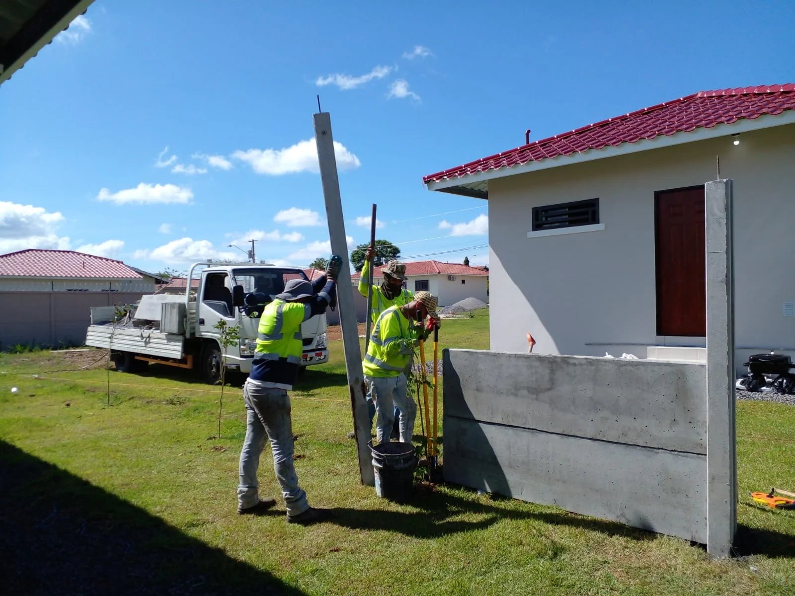 Operarios montando columnas verticales de muro perimetral prefabricado junto a vivienda terminada