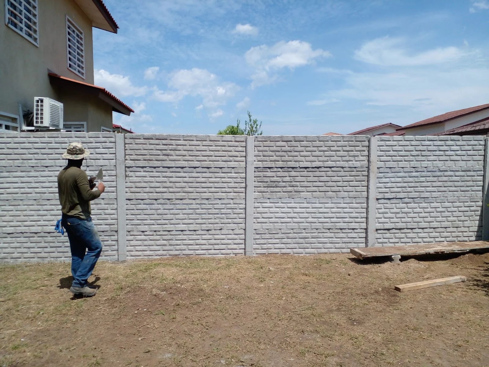 Operario inspeccionando muro perimetral con textura tipo bloque en residencia de dos plantas