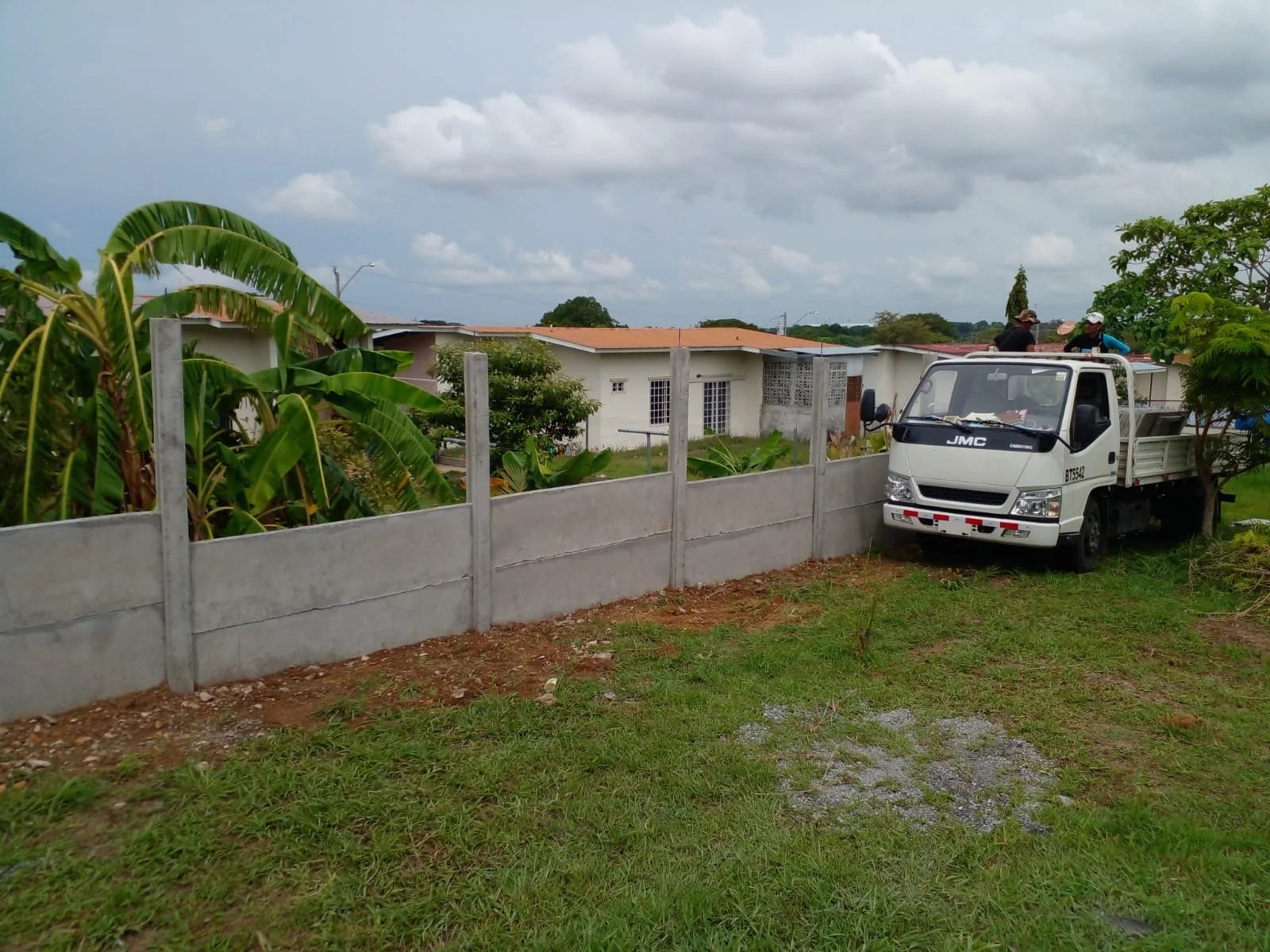 Muro perimetral prefabricado en lote residencial con camión y vegetación tropical al fondo