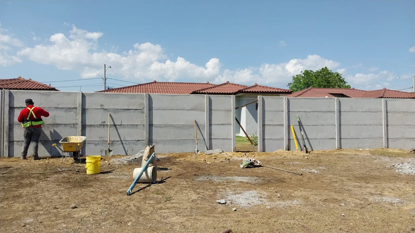 Lote con muro perimetral en construcción y operario al fondo junto a viviendas terminadas