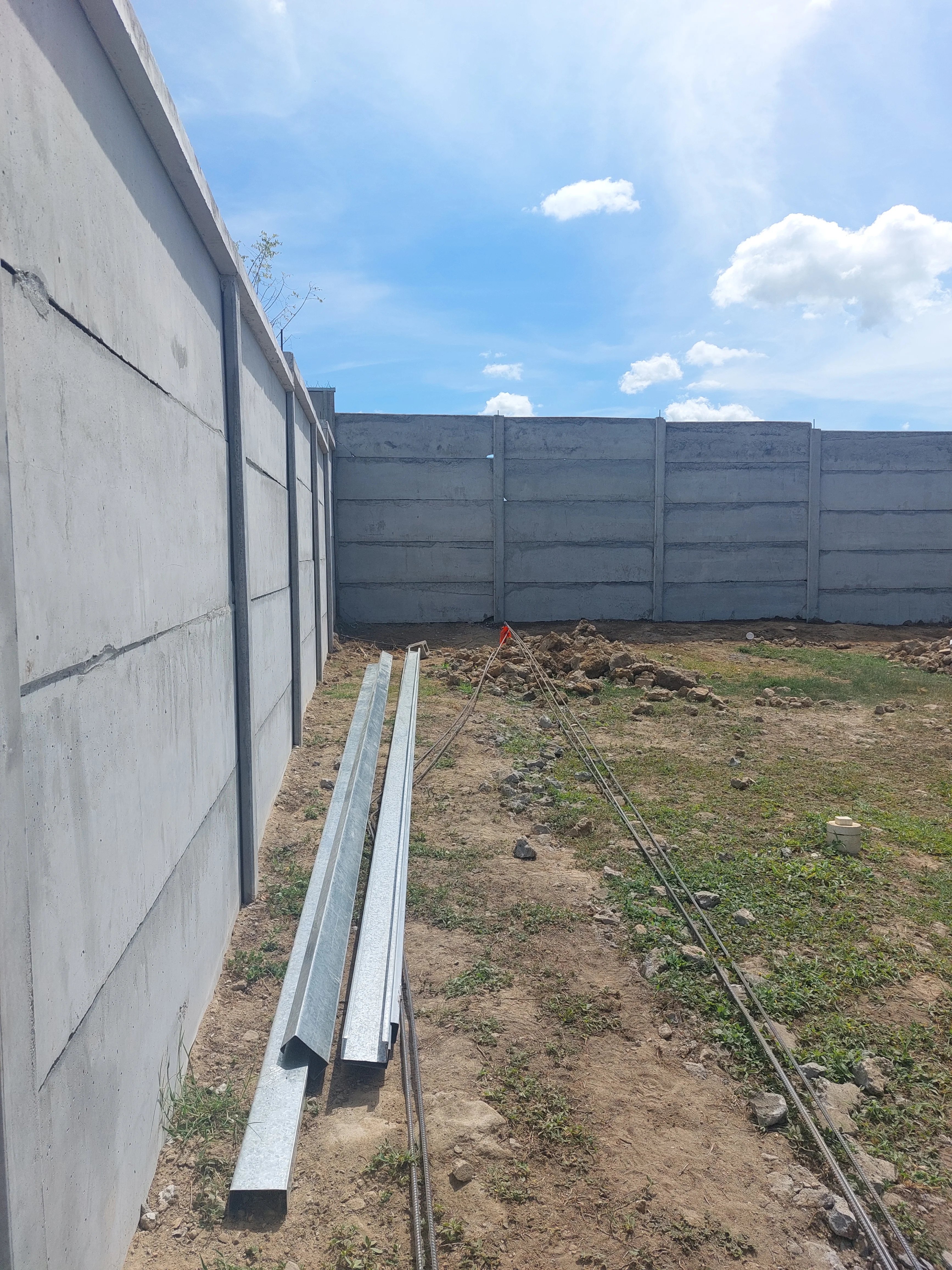 Muro perimetral prefabricado terminado con perfiles galvanizados apilados al pie en lote residencial