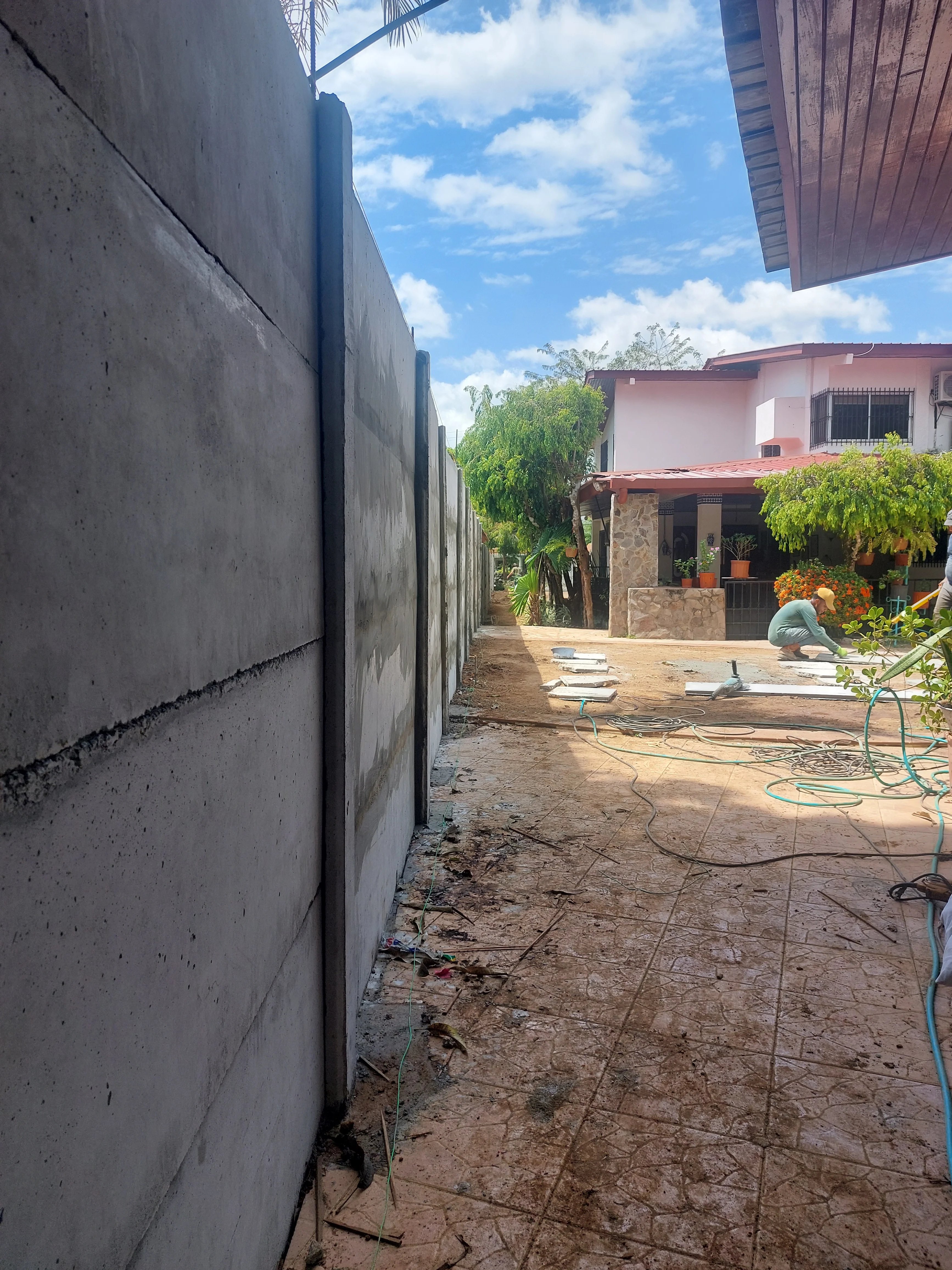 Vista lateral de muro perimetral prefabricado alto en residencia con vivienda y palmeras al fondo