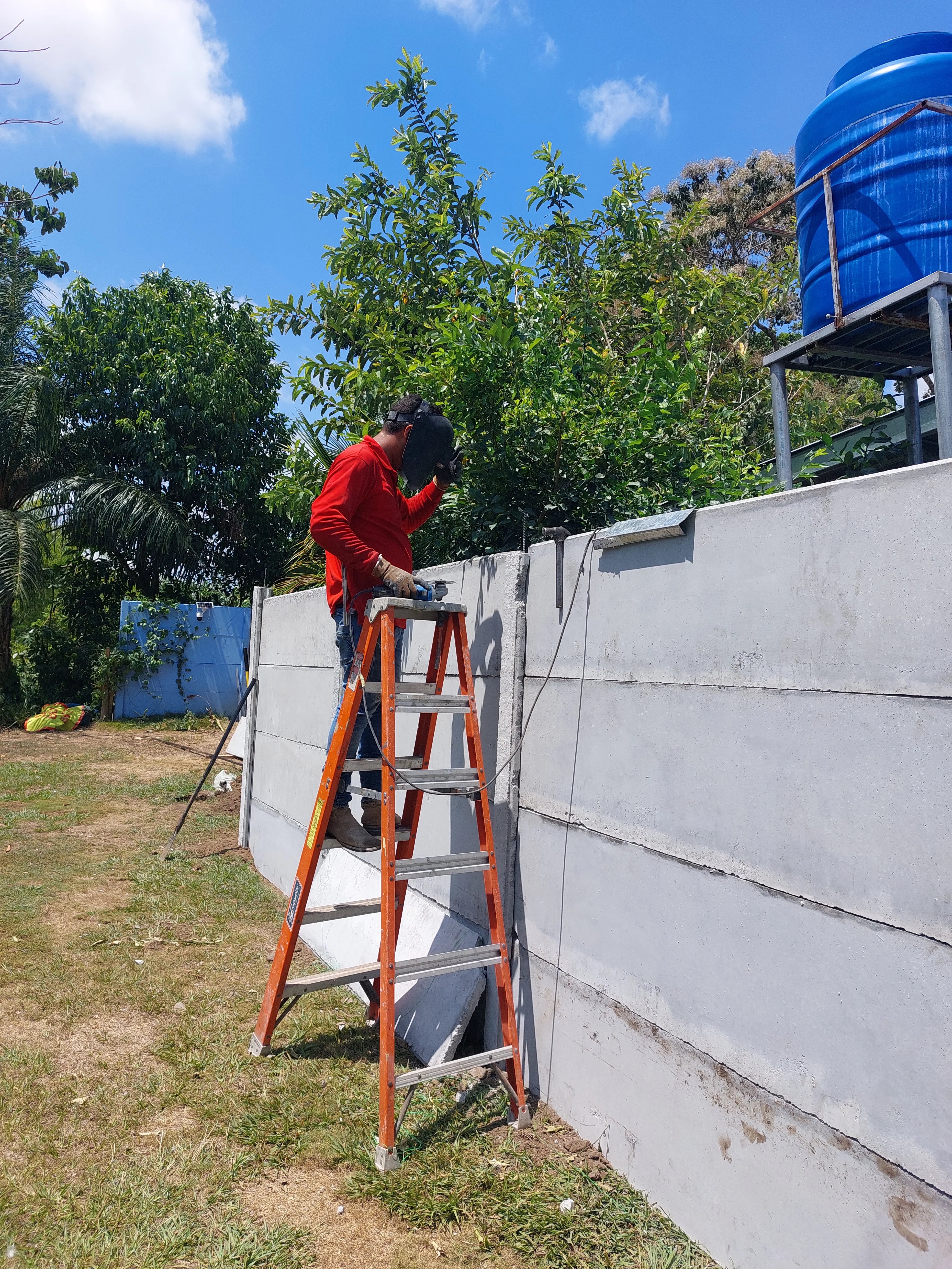 Operario sobre escalera realizando ajustes en la parte superior de muro perimetral prefabricado