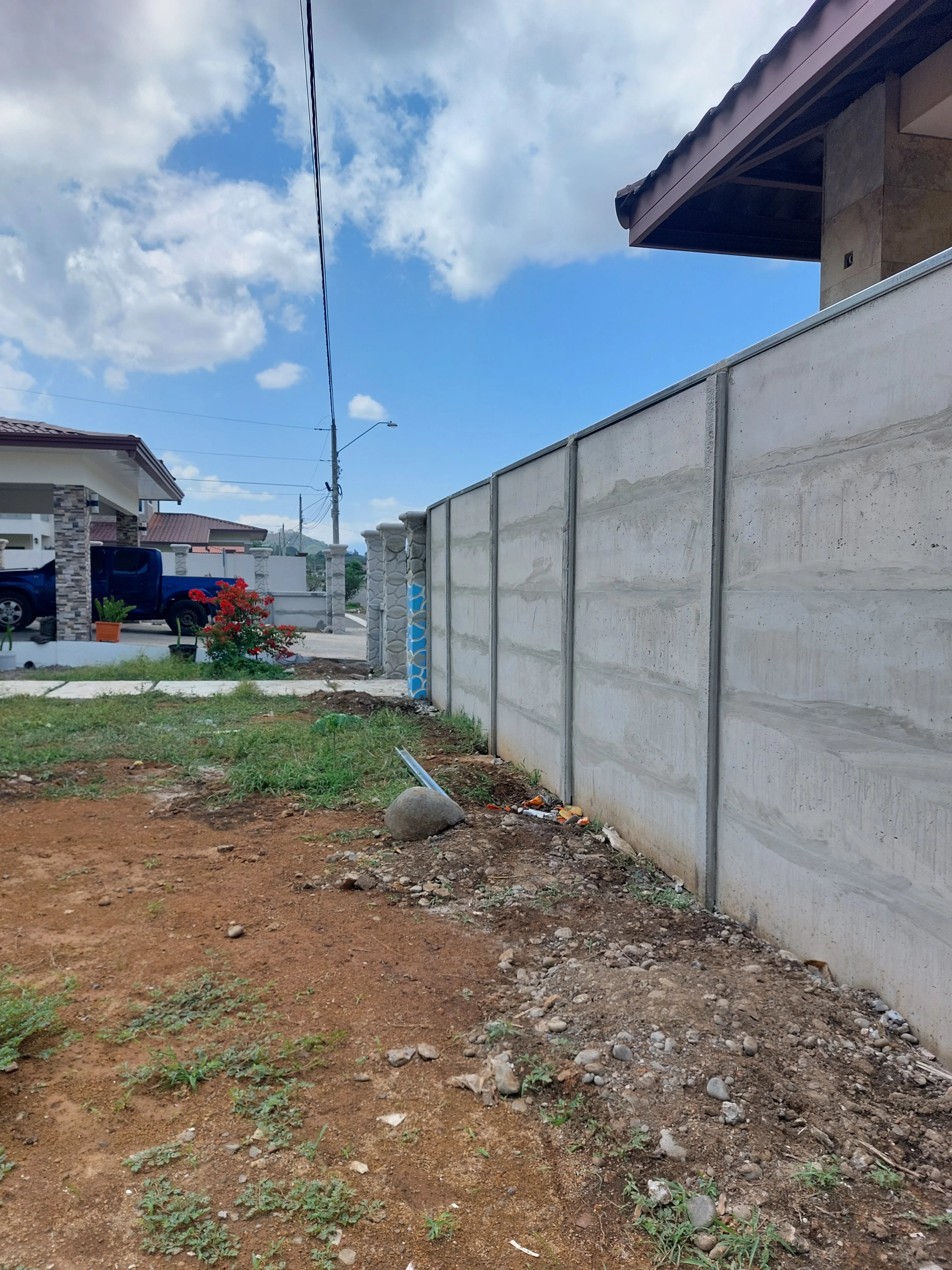 Muro perimetral prefabricado visto desde el interior de un lote vacío con residencia al fondo