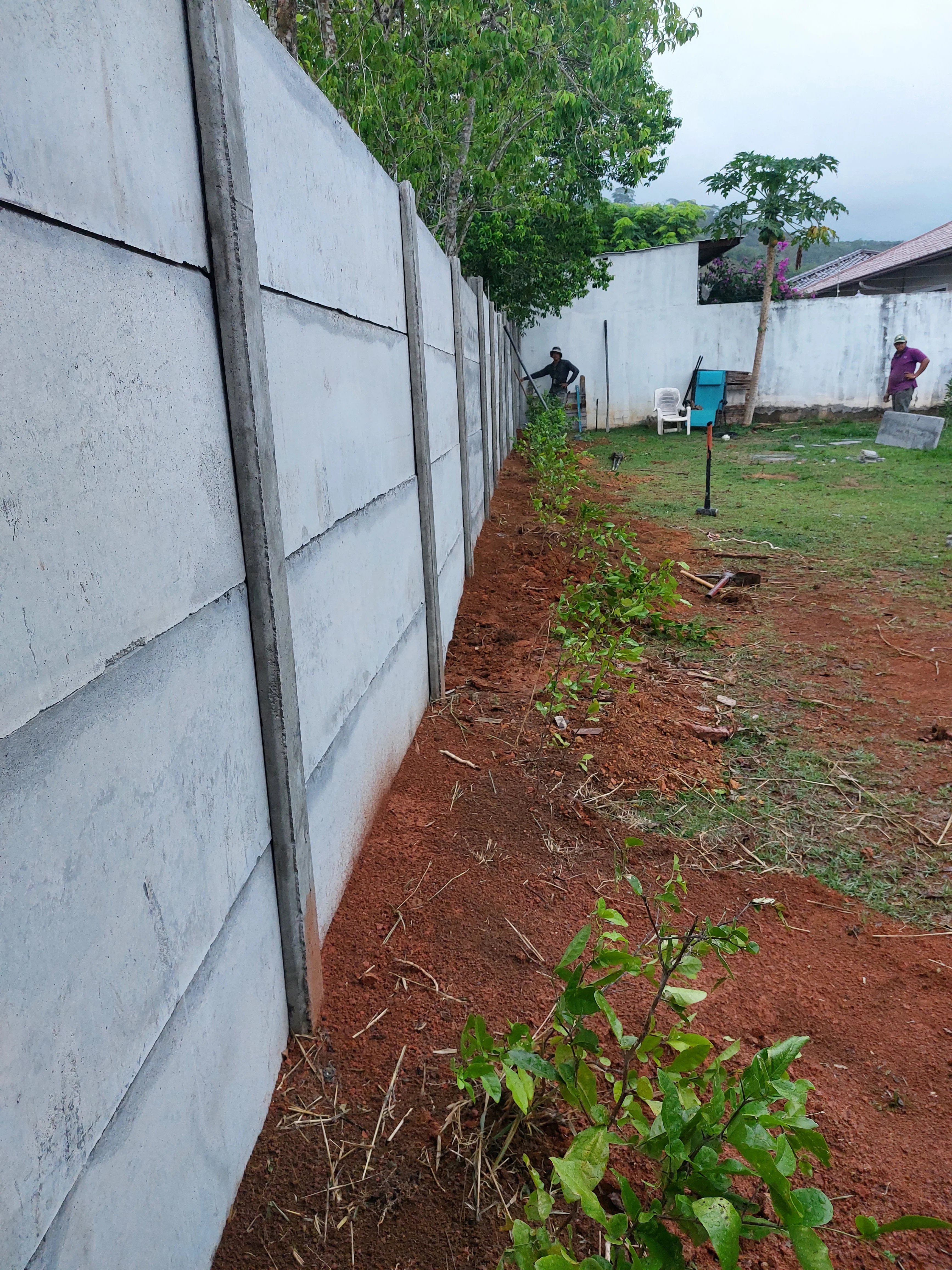 Muro perimetral prefabricado largo con cuadrilla trabajando paisajismo al fondo en residencia
