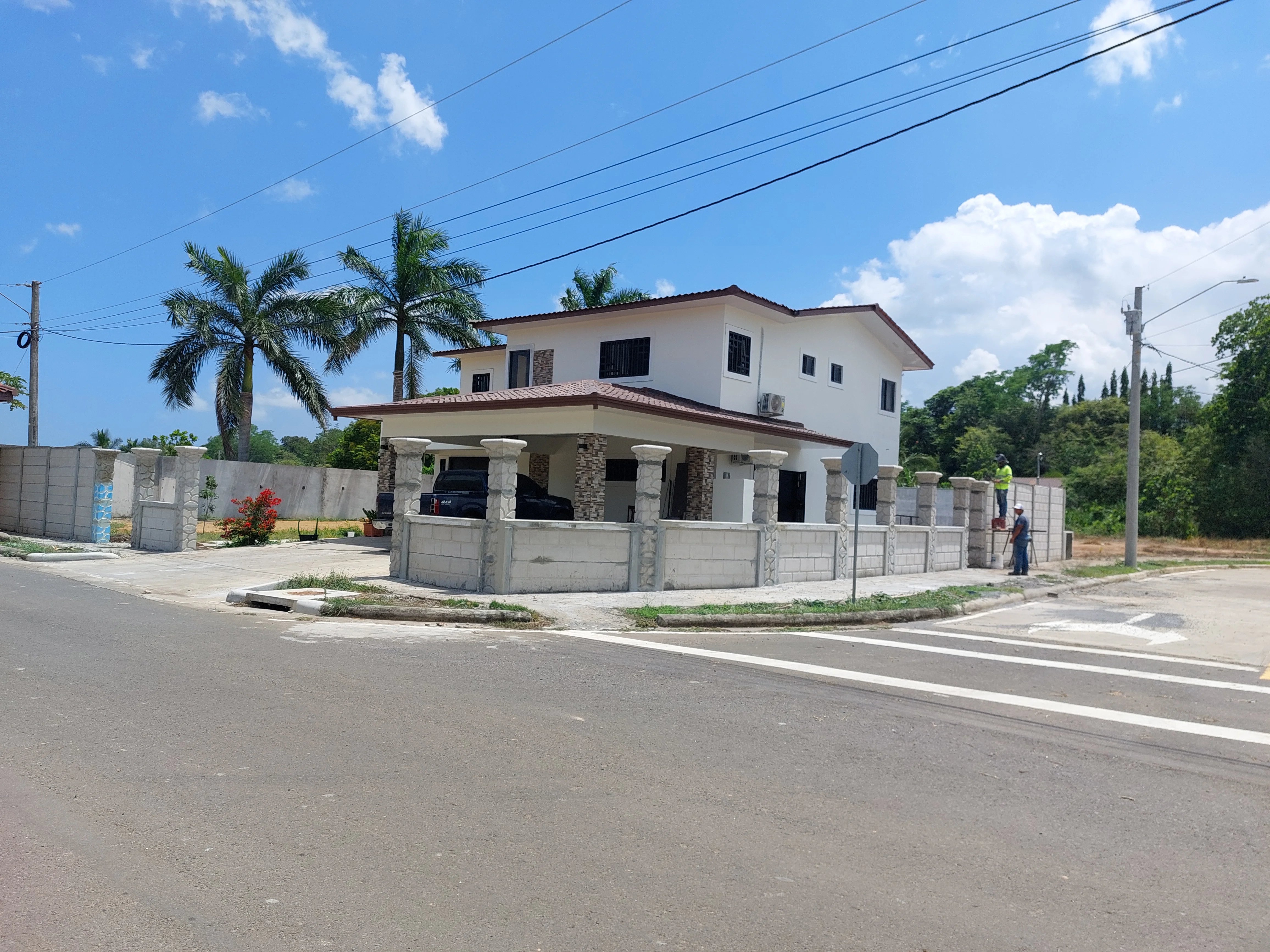 Residencia de dos plantas con muro perimetral prefabricado terminado y palmeras en zona urbana