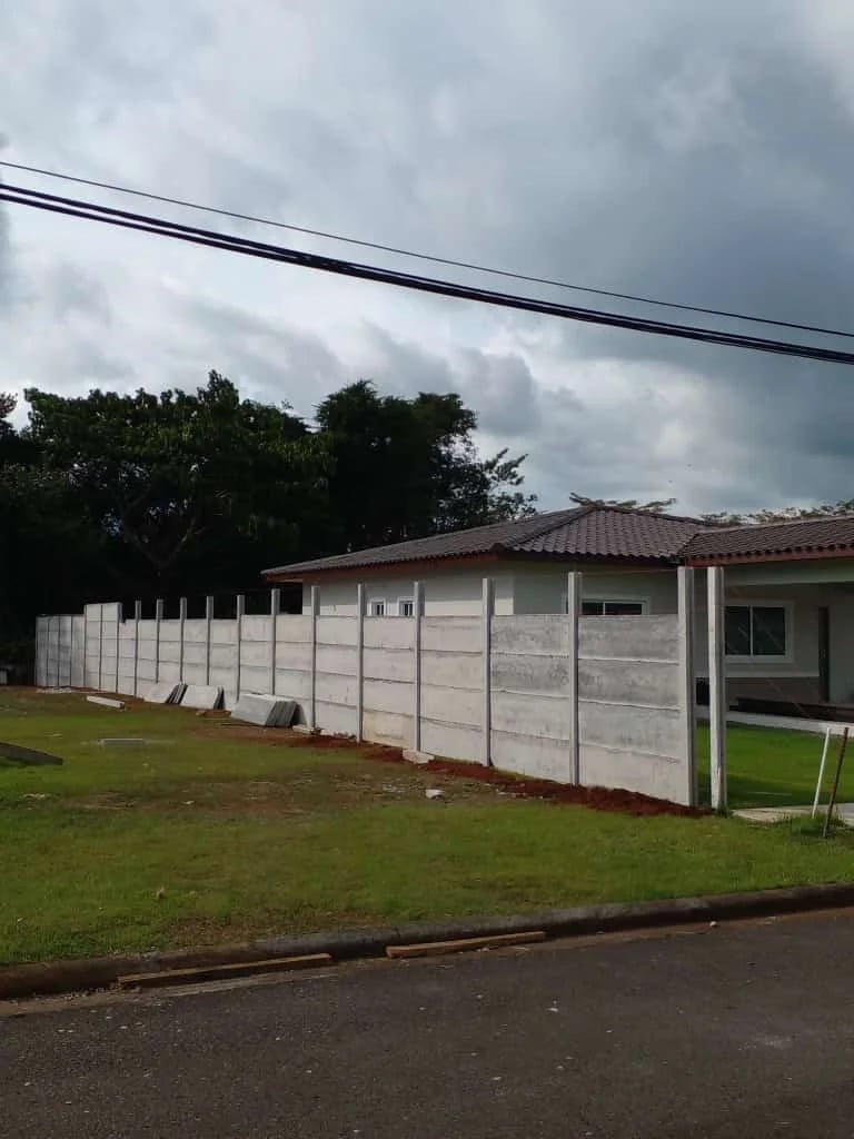 Muro perimetral prefabricado largo con perspectiva en frente de vivienda y calle pavimentada