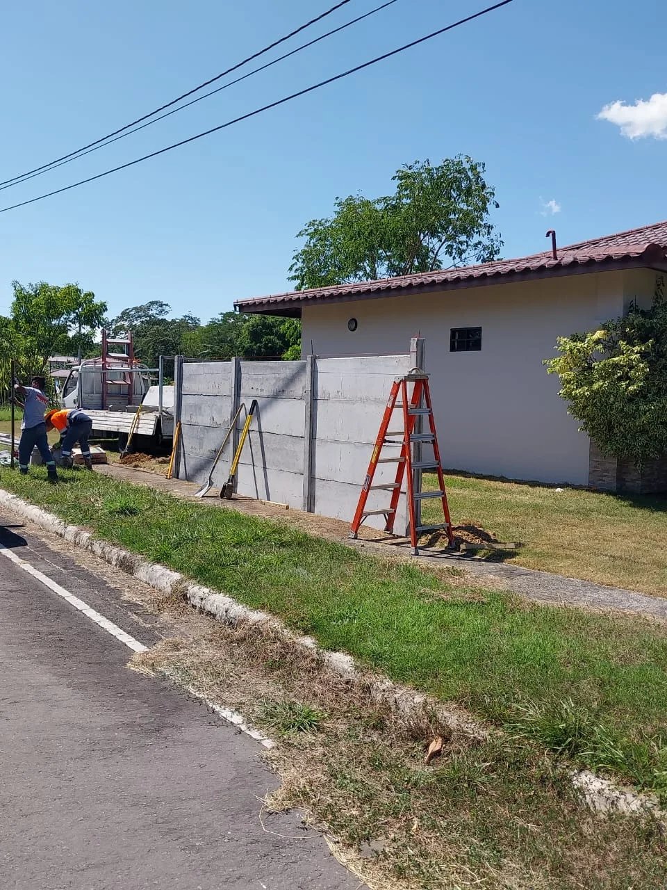 Operario instalando muro perimetral con escalera junto a vivienda en zona urbana arbolada