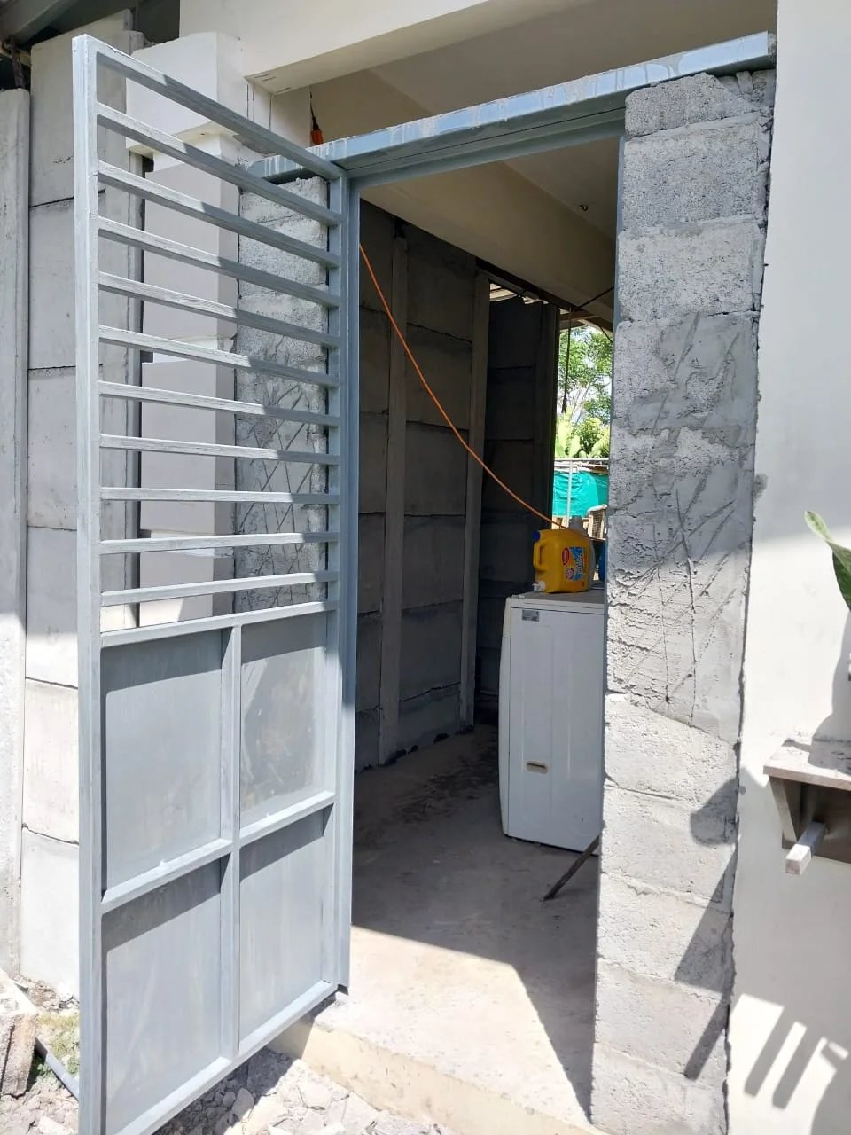 Puerta metálica gris instalada en cuarto de servicio con muros de bloque a la vista