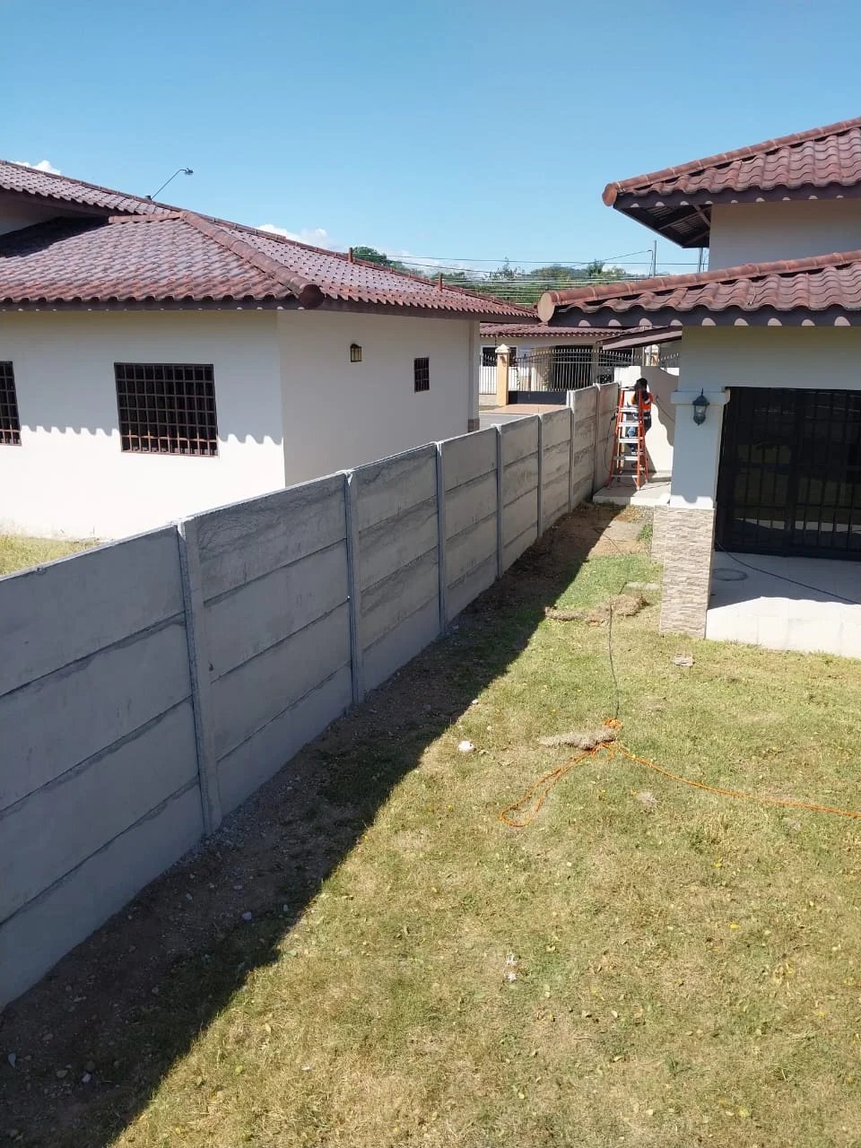 Muro perimetral prefabricado entre residencias con vivienda de techo de teja al fondo