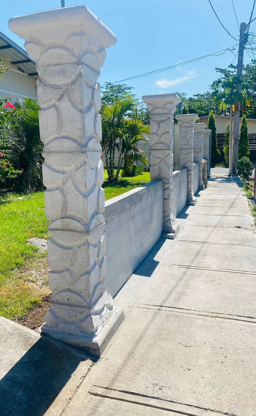 Columnas decorativas prefabricadas con relieve geométrico sobre muro bajo frente a residencia